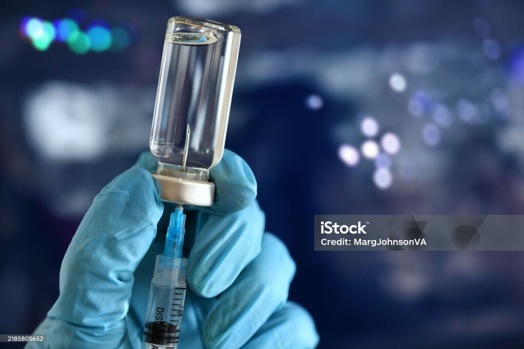 Medical personnel filling a syringe needle with generic vaccine booster from vial