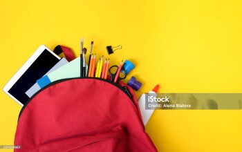 Red school backpack filled with glue, pencils, tablet, brushes, clips and notebooks on yellow. Great image for back to school sales, children’s education, and classroom promos.