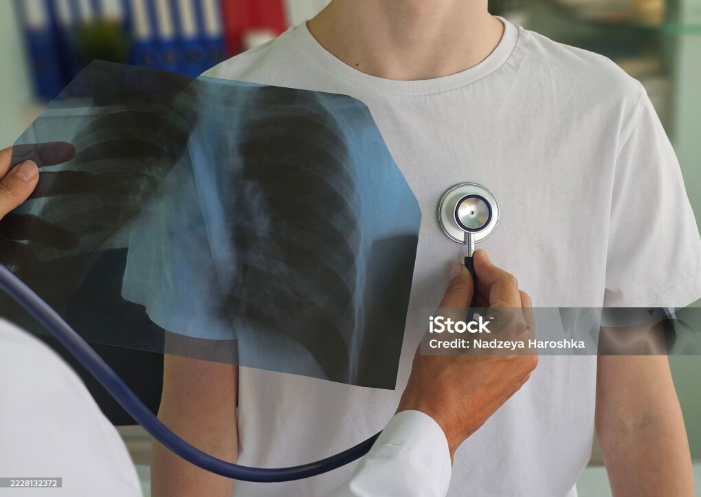 Doctor examines patient using stethoscope while reviewing X-ray in a medical office