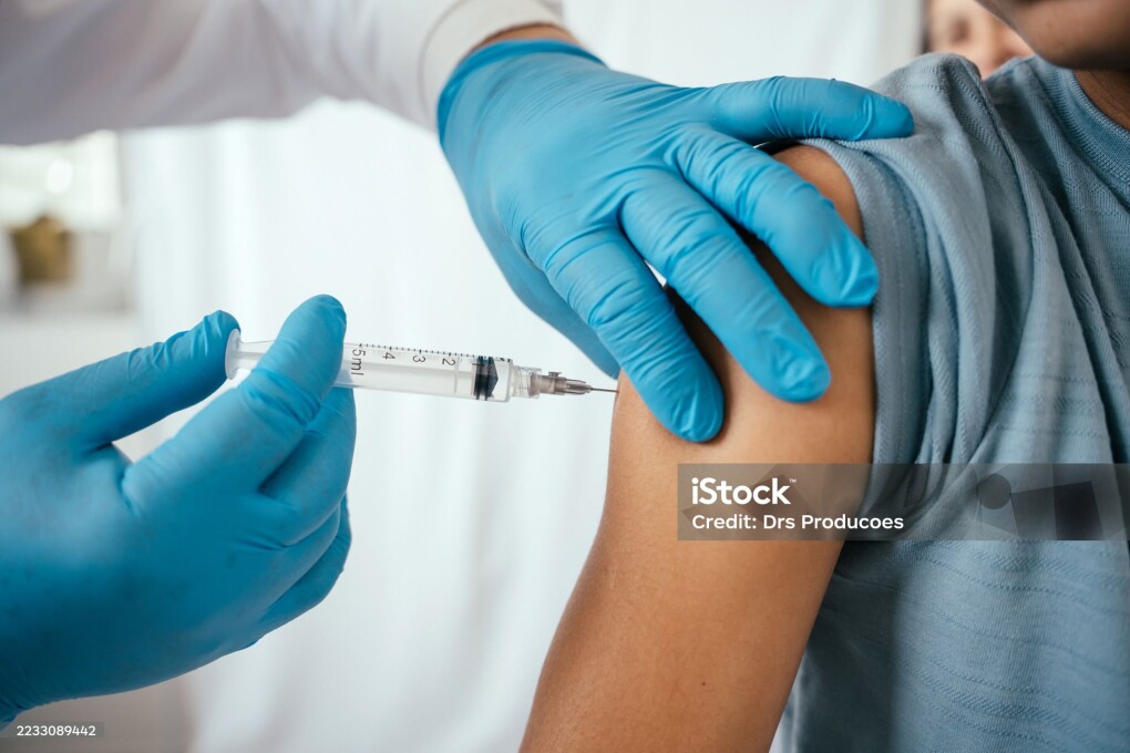 Doctor administering vaccine to teenager in doctor's office