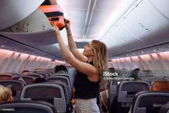 Woman travel by airplane. Passenger putting hand baggage in lockers above seats of plane.  hands are seen placing or retrieving a pink hard-shell suitcase from an airplane's overhead storage compartment.