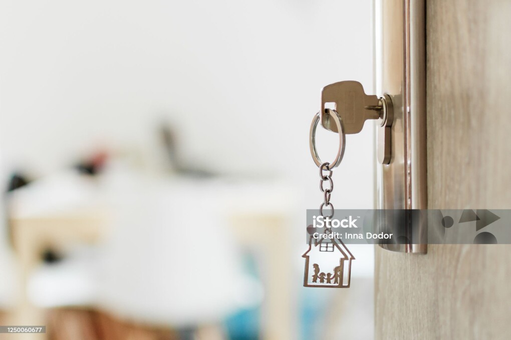 Key with keychain in a house shape and family in the door keyhole. Buy new home concept. Real estate market.