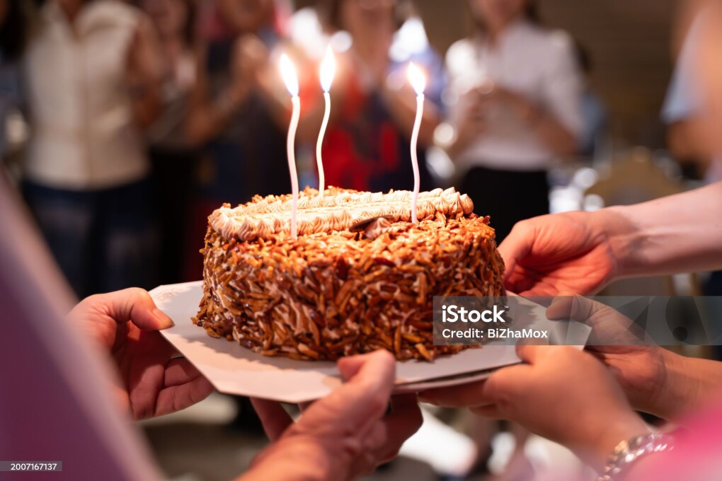 Hands of young people holding a happy birthday cake with their friends Candle flame lights on birthday cake during celebration.