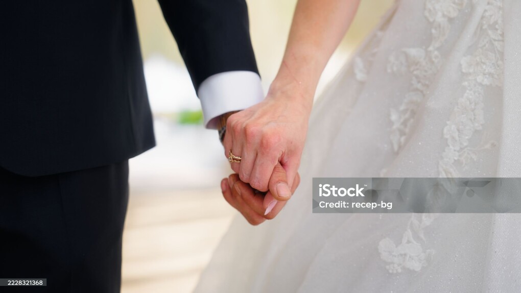 A close-up video of newlywed, young bride and groom, holding each other's hands. The wedding ring is visible in the shot.
