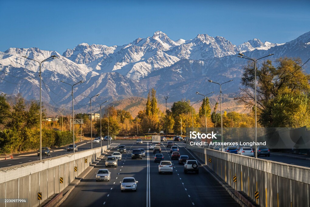 Almaty city street and busy highway with autumn trees, traffic, and the snow-capped Trans-Ili Alatau mountains in Kazakhstan largest city.