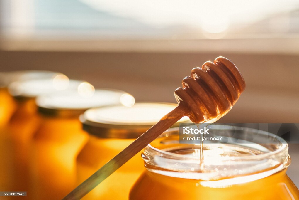 Honey dipper and open glass of honey.