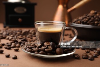 Cup of hot coffee, cezve, grinder and beans on brown background, closeup