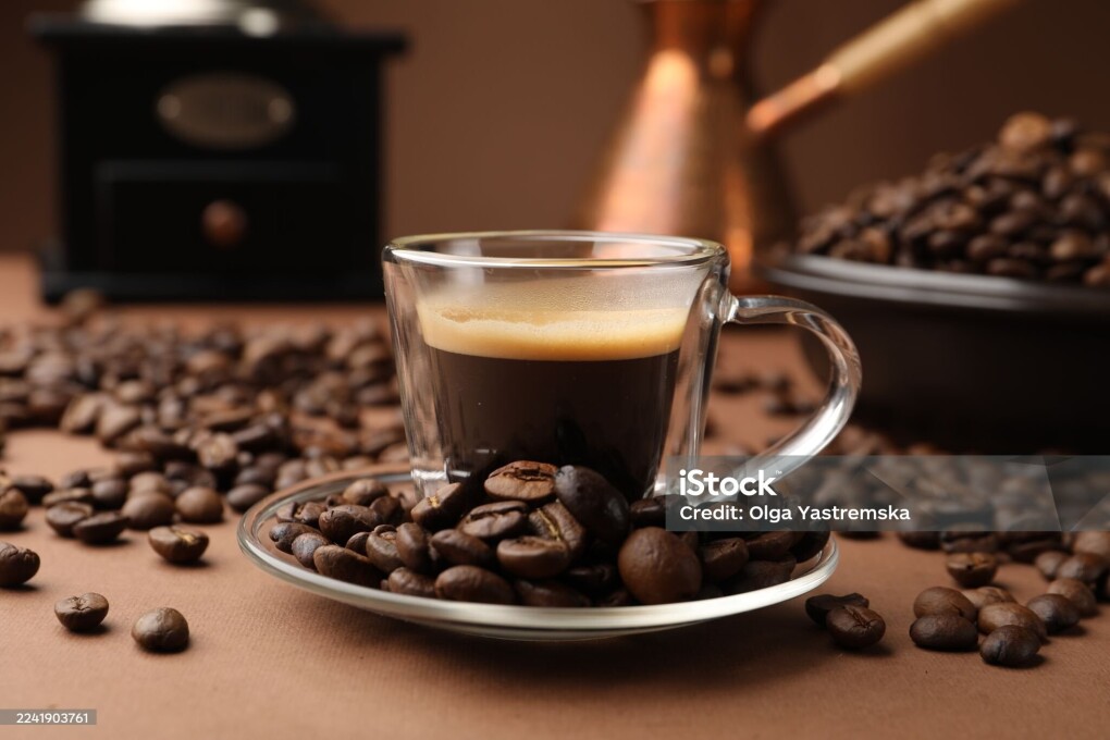 Cup of hot coffee, cezve, grinder and beans on brown background, closeup