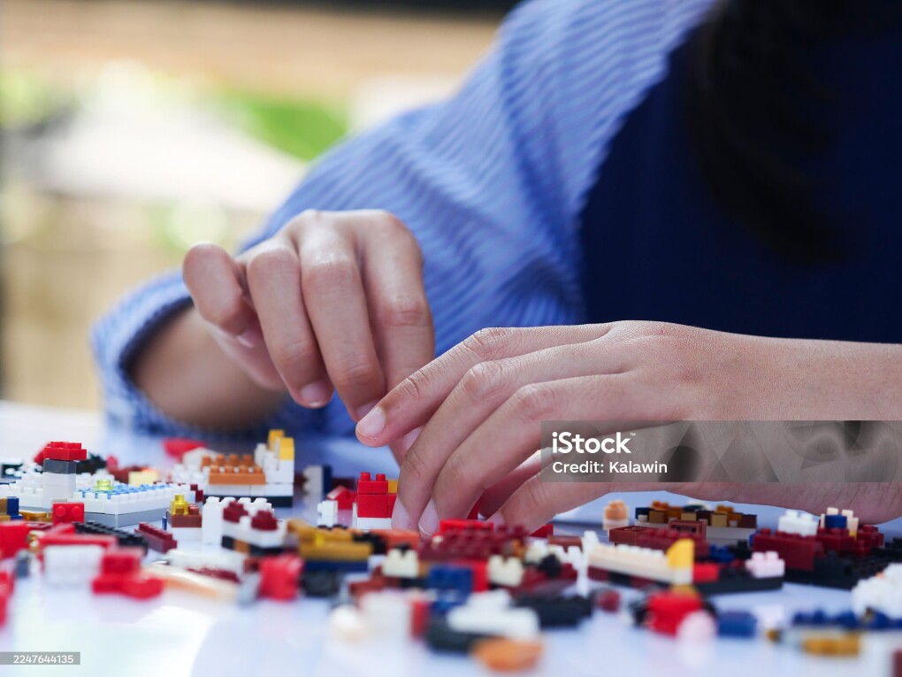 Children hands play with colorful plastic building block blocks on white table.