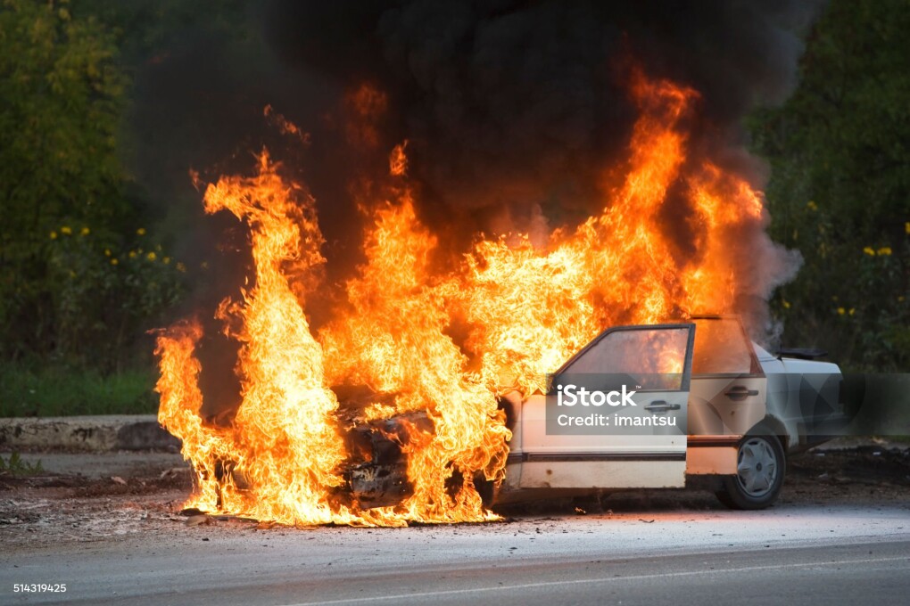 The car is burning on the roadway.
