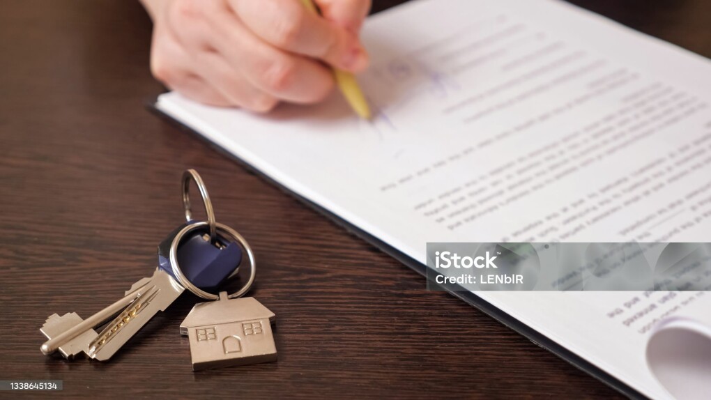 Man client signs new apartment purchase contract with pen near keys with house shaped breloque put on table extreme close view