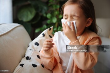 Sick little schoolgirl coughs and blows nose wiping with white paper napkin.