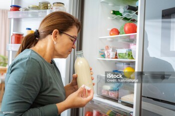 Disgusted woman smelling expired milk by the fridge