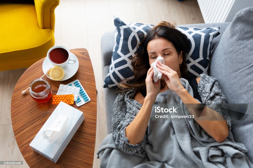 Woman is laying on a couch with a tissue in her mouth. A cup of tea is on a table next to her