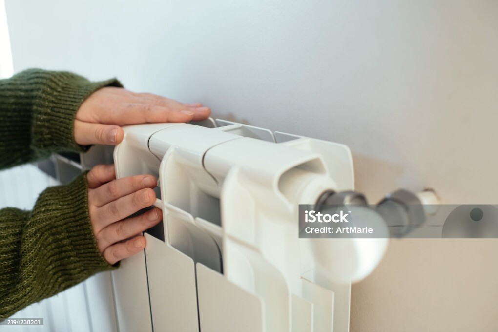 Young woman trying to warm near a radiator in winter, close-up