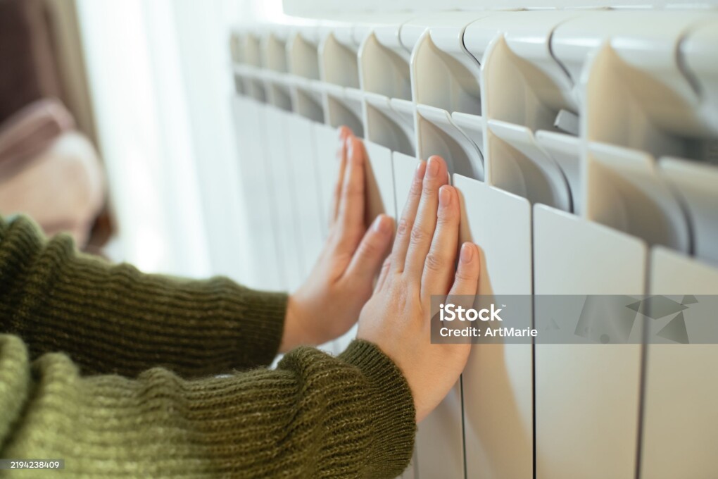 Young woman trying to warm near a radiator in winter, close-up