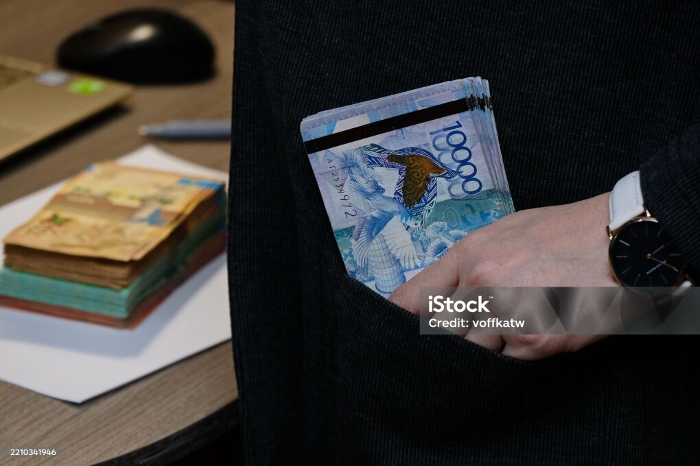 A woman holds tenge banknotes of different denominations in her hands.
