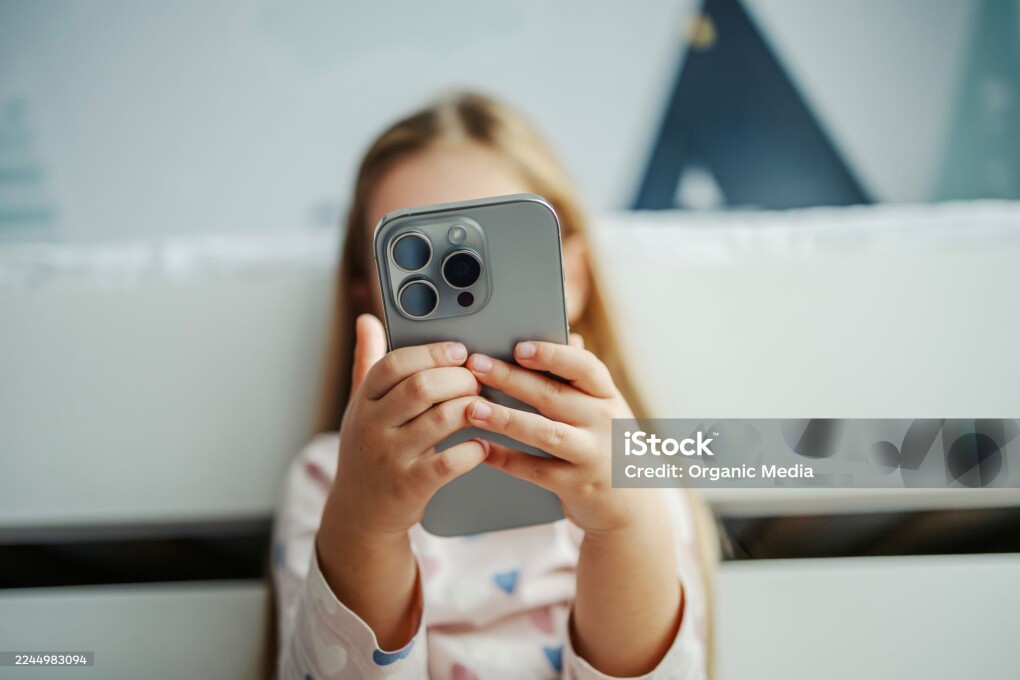 Child's hands holding a modern smartphone covering face. Focusing on technology, screen time, and digital native youth
