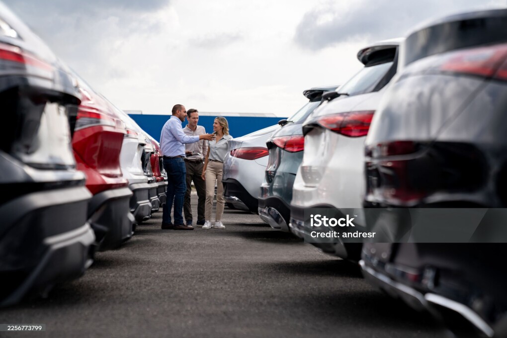 Happy Latin American car salesperson showing cars to a couple shopping at the dealership